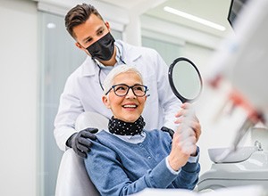Woman in dental chair smiling at reflection with dentist touching her shoulders