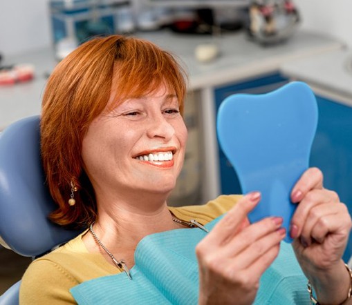 Woman in patient’s chair smiling in small mirror