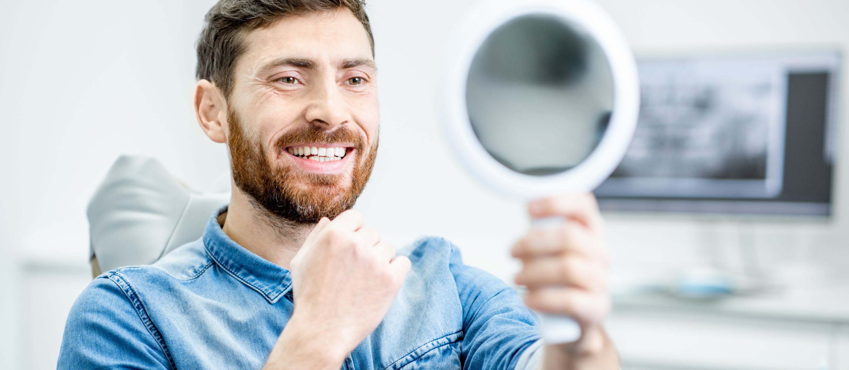 Man in dental chair admiring his smile in a mirror after cosmetic dentistry in Boynton Beach